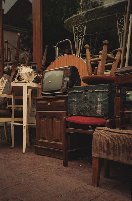 A collection of vintage and retro suitcases and storage chests stacked outside a shopfront, alongside a red metal cooler with the brand name